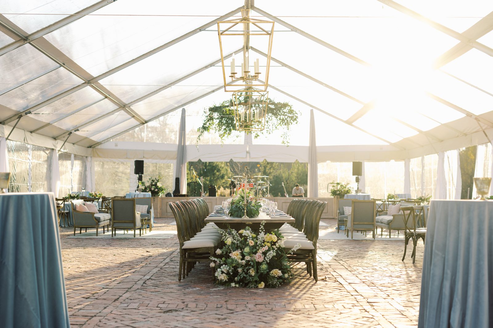 Clear-top tent reception with a crystal chandelier, hanging greenery, and a floral farm table