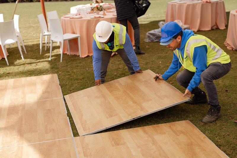 Classic Tents & Events crew installing wood-look event flooring panels on a lawn