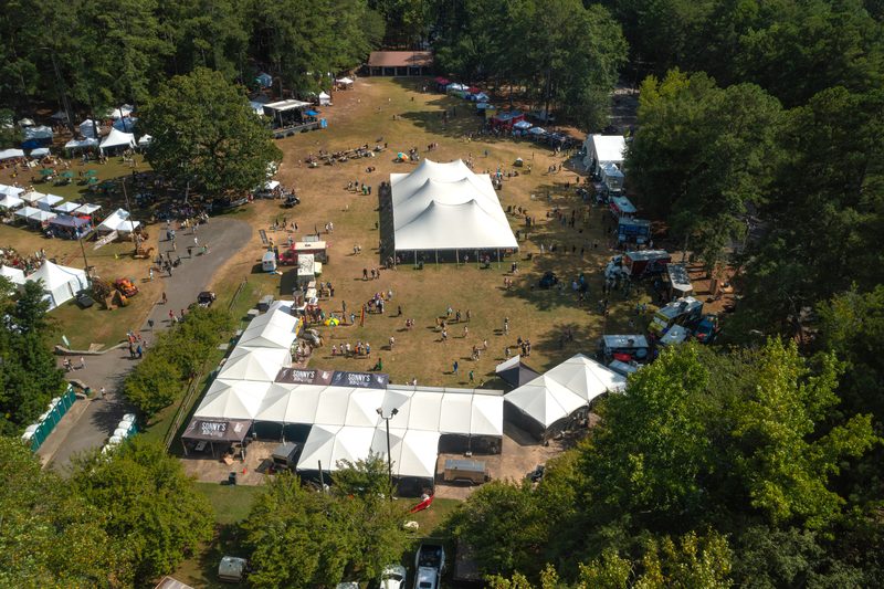 Aerial view of a festival ground with large white tents among the trees