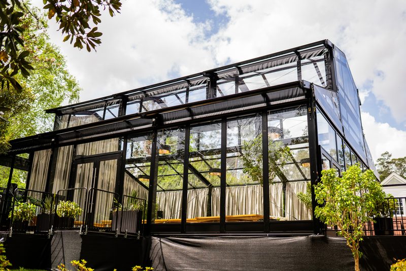 Black-framed glass event enclosure with sheer drapery set up outdoors