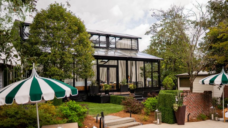 Glass event structure with green and white market umbrellas on a garden patio