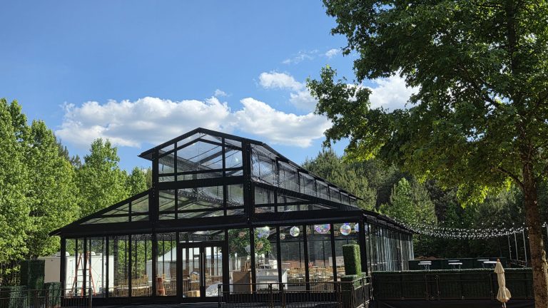 Black-framed glass event structure under the trees on a sunny day