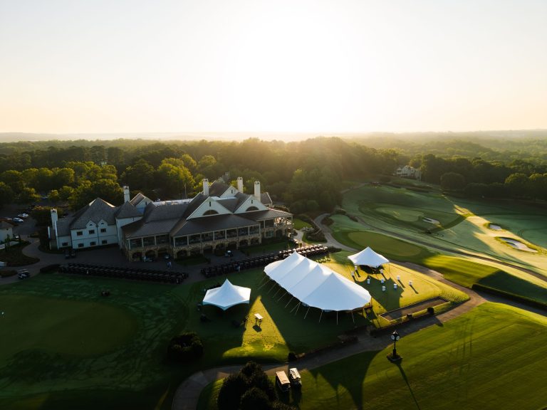 Aerial view of Classic Tents & Events pole tents set up beside a golf clubhouse at sunrise