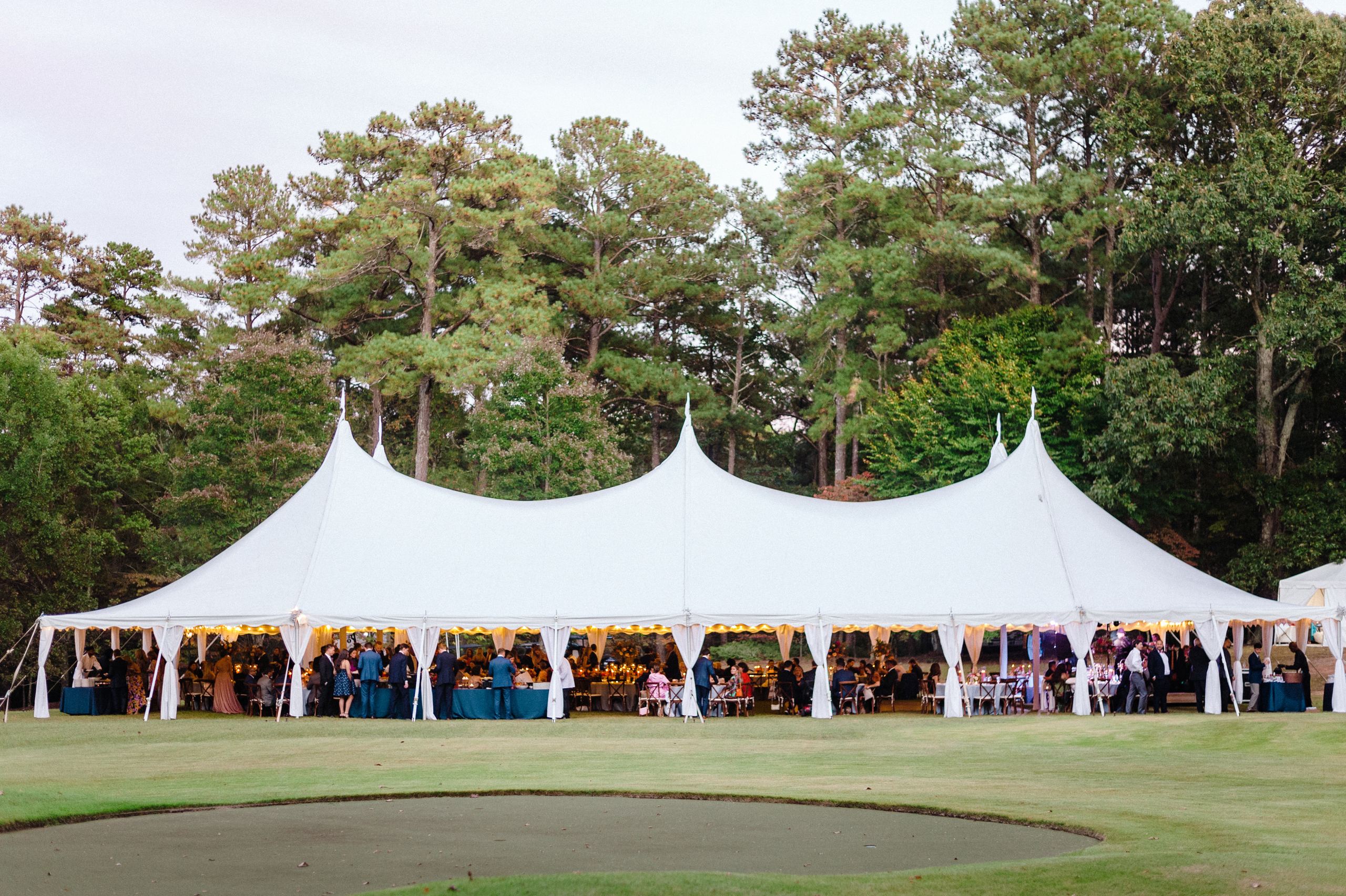 Large white high-peak pole tent hosting an evening event on a golf course