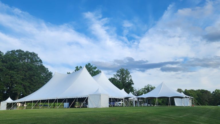 White high-peak pole tents set up on an event lawn under a blue sky