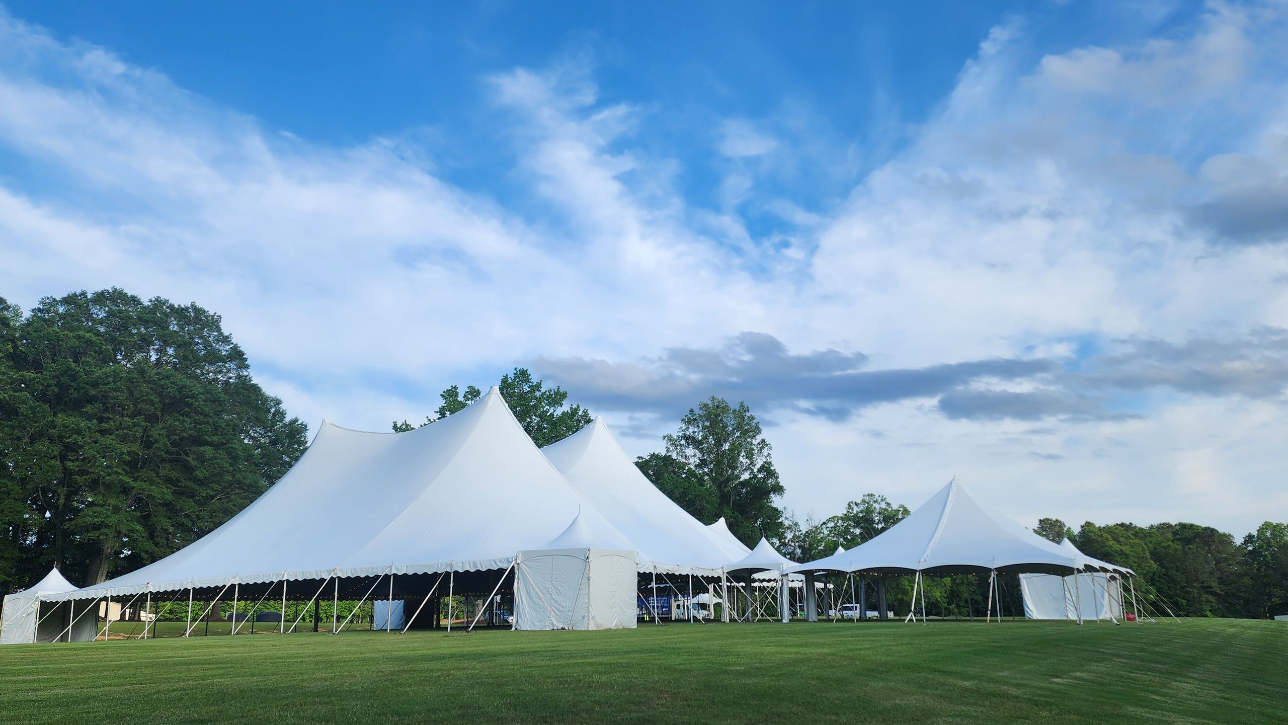 White high-peak pole tents set up on an event lawn under a blue sky