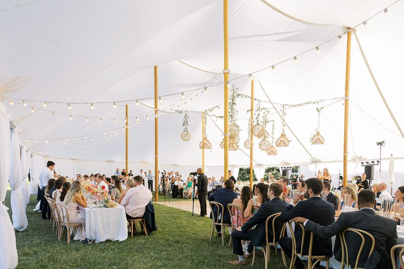 Wedding guests dining under a sailcloth tent with string lights and wooden center poles