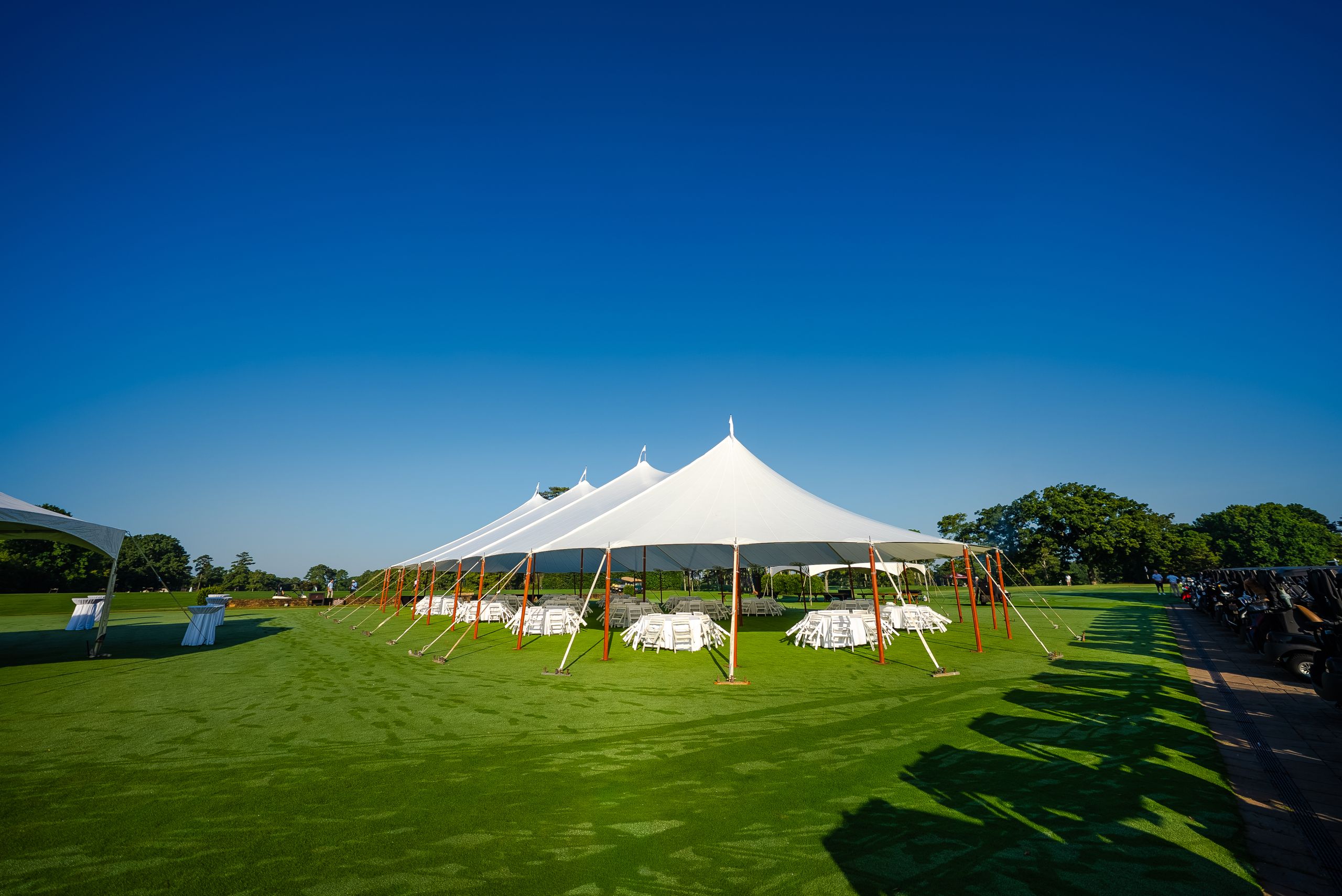 White sailcloth tents with wooden poles set up on a lawn under a deep blue sky